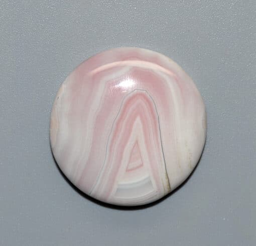 A pink and white agate button on a gray surface.