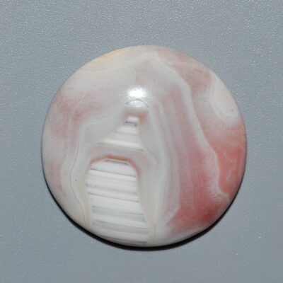 A white and pink agate button on a gray surface.