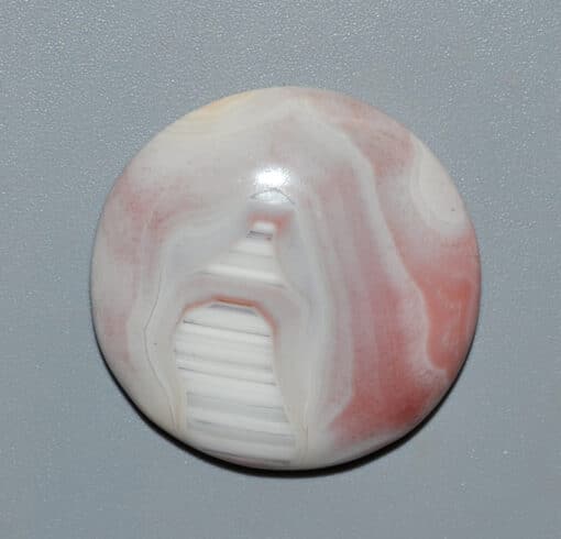 A white and pink agate button on a gray surface.