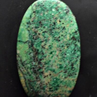 A green stone cabochon on a black surface.