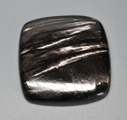 A black square shaped stone with black streaks on it.