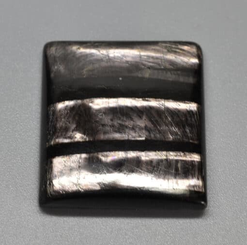 A square piece of black labradorite on a grey surface.