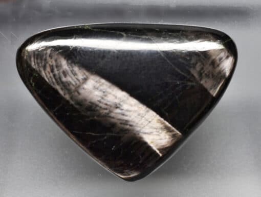 A black triangular shaped stone on a white surface.