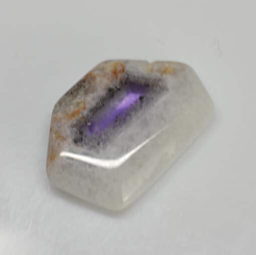 An amethyst cabochon on a white surface.