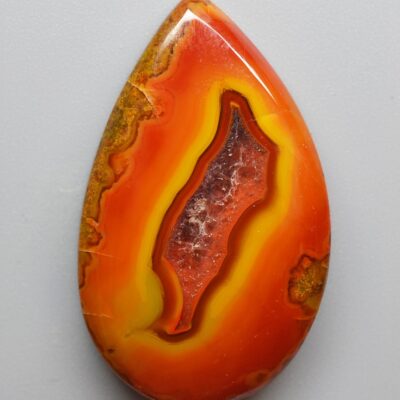 A red and orange agate pendant on a white surface.