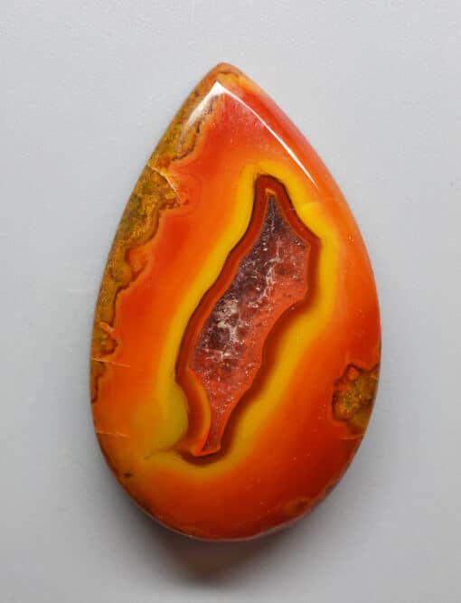 A red and orange agate pendant on a white surface.