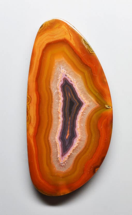 An orange and purple agate piece on a white surface.