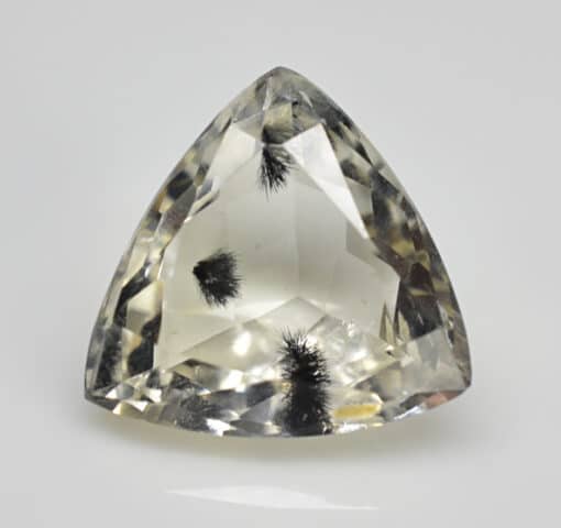 A triangular shaped yellow topaz on a white surface.