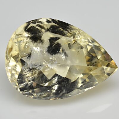 A pear shaped yellow topaz on a white surface.