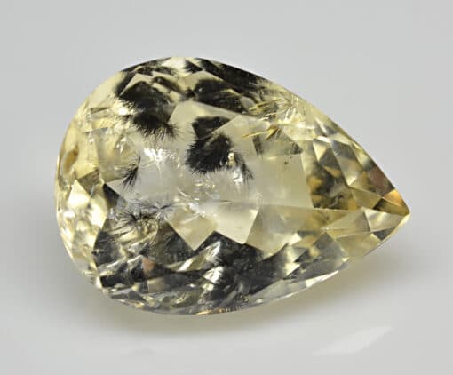 A pear shaped yellow topaz on a white surface.