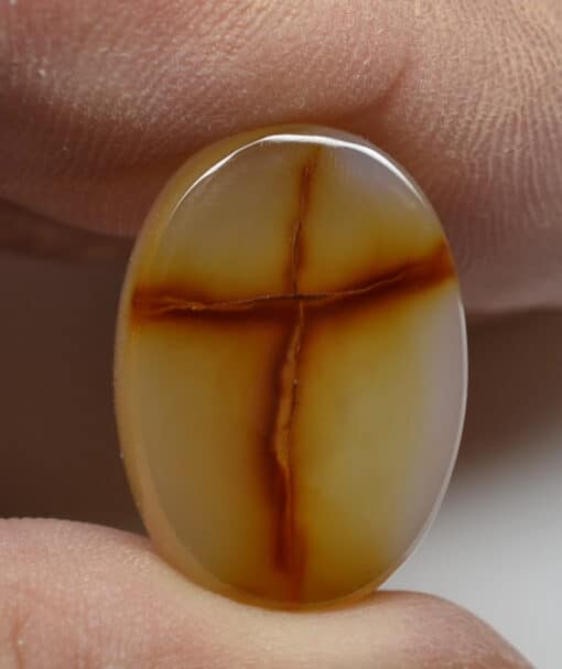 A person holding an agate stone with a cross on it.