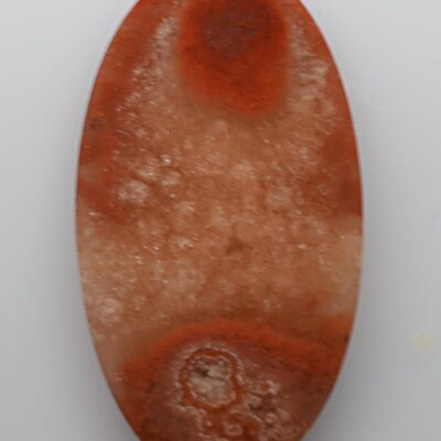 An oval piece of red agate on a white surface.