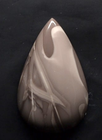 A brown and white marbled teardrop on a black surface.