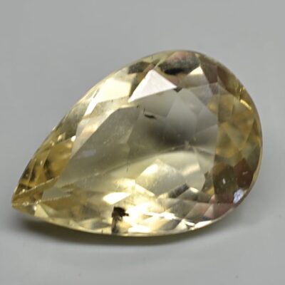 A pear shaped yellow sapphire on a white surface.