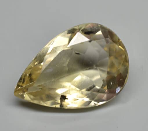 A pear shaped yellow sapphire on a white surface.