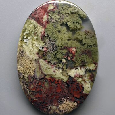 A green, red, and brown stone is displayed on a gray surface.