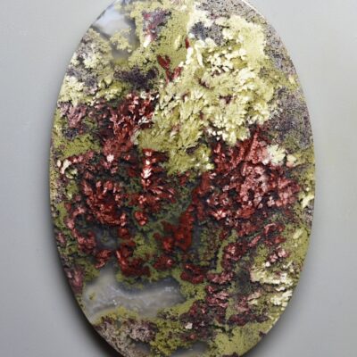 A round piece of stone with red and green moss on it.
