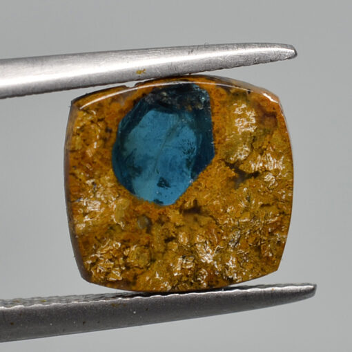 A blue topaz stone is being held by a pair of pliers.