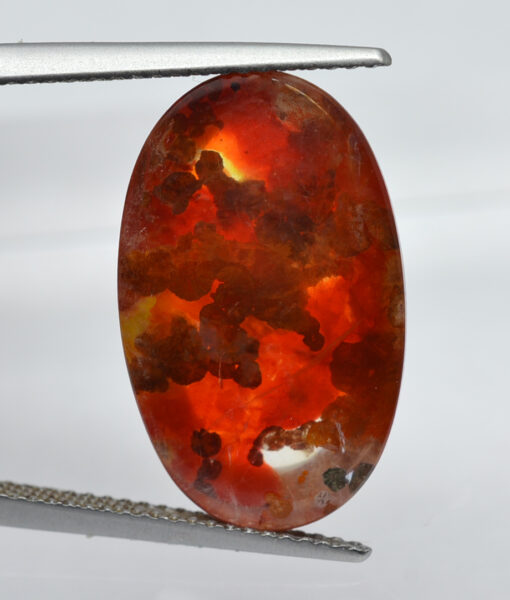 An orange apatite stone is being held by a pair of pliers.