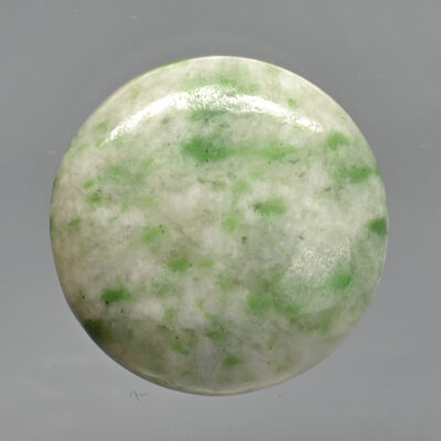 A green jade button on a gray surface.
