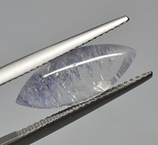 A blue sapphire stone being cut with a pair of tweezers.