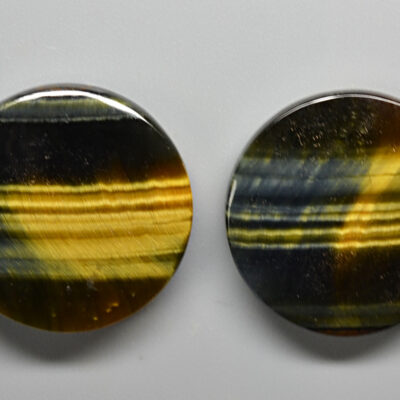 Two oval tiger eye cabochons on a white surface.