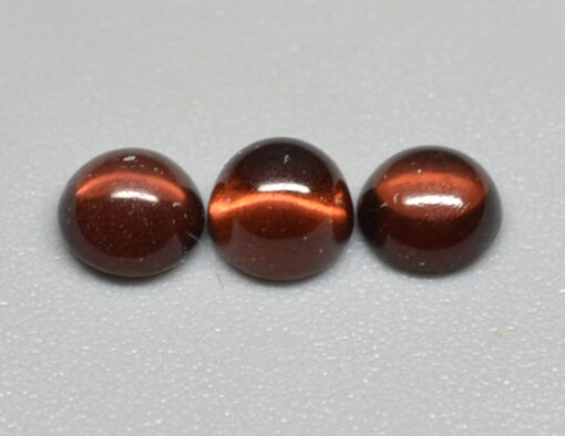 Three brown tiger eye beads on a white surface.