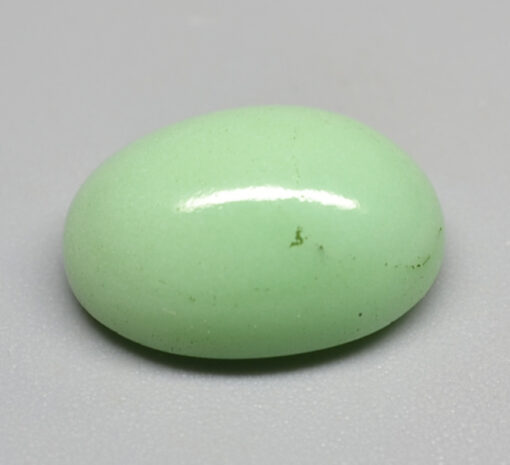 An oval green jade stone on a white surface.