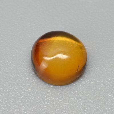 A yellow tiger eye stone on a grey surface.