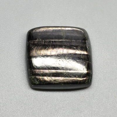 A square black labradorite cabochon on a white surface.