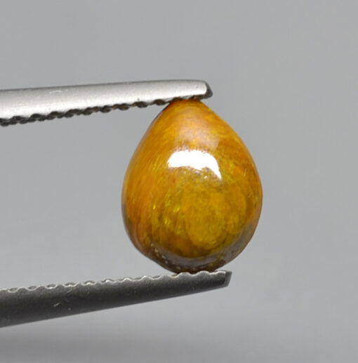 A yellow tear shaped stone being held by a pair of pliers.