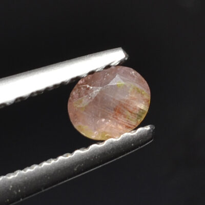 A piece of a pink sapphire with a piece of tweezers.