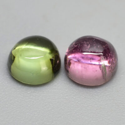 Two pink and green gemstones on a white surface.