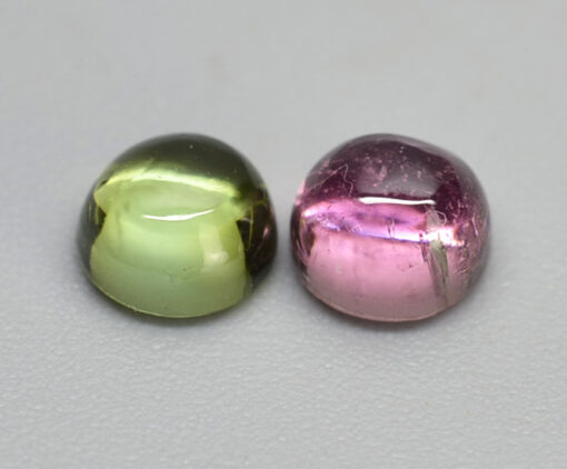 Two pink and green gemstones on a white surface.