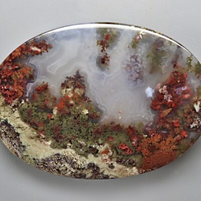 A piece of Indonesian Moss Agate 116.80 ct Oval Cabochon 61.00 x 41.00 x 6.00 mm max3085 on a white surface.