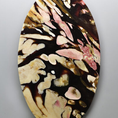 An oval shaped piece of art with black and pink paint on it.