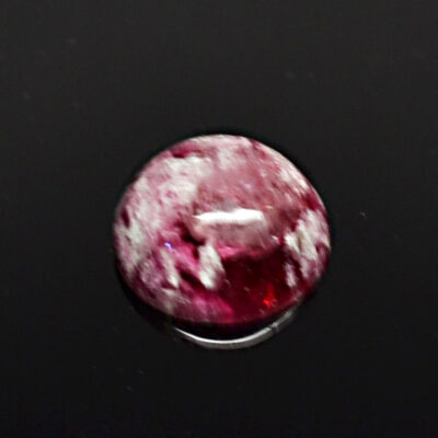 A round ruby stone on a black surface.