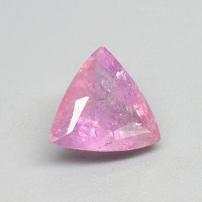 A pink sapphire triangular shaped stone on a white surface.