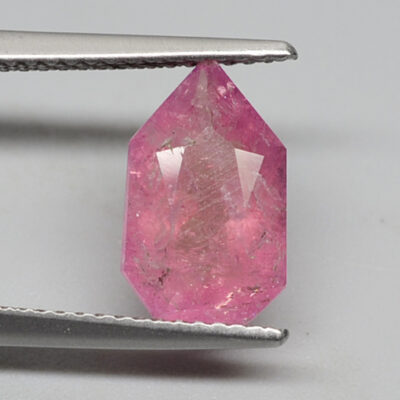 A pink sapphire stone being cut with a pair of pliers.