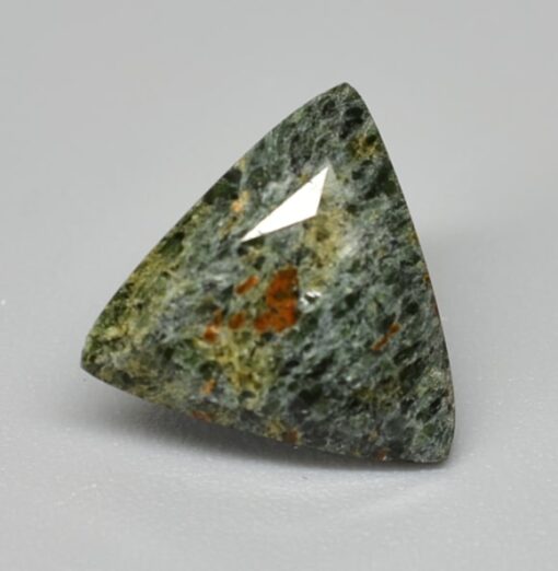 A triangular green jade stone on a white surface.