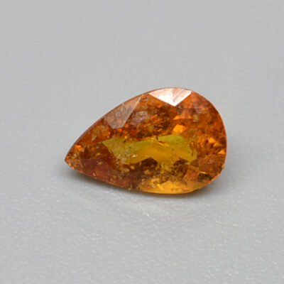 A pear shaped orange sapphire on a white surface.
