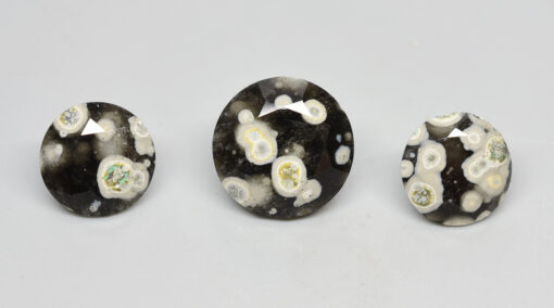 Three pieces of black and white apatite on a white surface.
