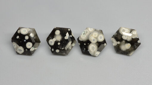 A group of black and white hexahedral cabochons on a gray surface.