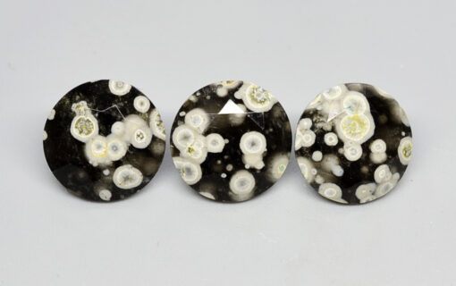 Three black and white apatite cabochons on a white surface.