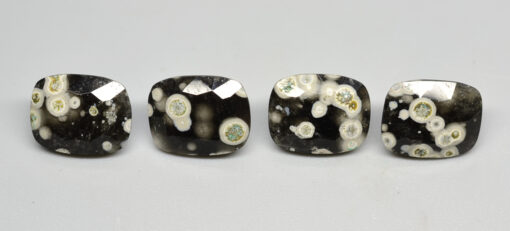 Four black and white apatite cabochons on a white surface.
