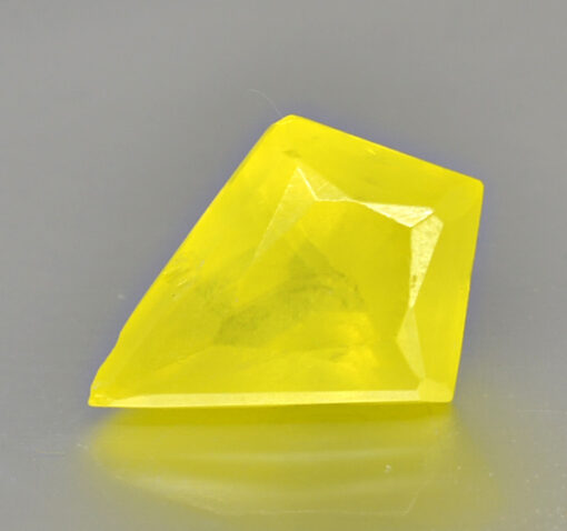 A yellow diamond, valued at $100 or more, cut on a gray surface.